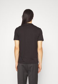 Svart bomullströja med korta ärmar och rundad halsringning, visad bakifrån. Slät textur, åtsittande stil.