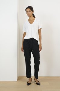 T-shirt bianca a scollo a V abbinata a pantaloni neri con cordoncino e décolleté neri. Design semplice con texture lisce, adatto per un abbigliamento casual.
