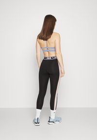 Lichtblauwe sportbeha met meerdere banden, gecombineerd met zwarte leggings met een roze zijstreep en een gebrandmerkte tailleband. Atletiekschoenen inbegrepen.