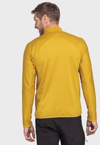 Langärmlige, figurbetonte gelbe Jacke mit strukturiertem Rippmuster, hohem Kragen und Flachnähte, von hinten betrachtet.