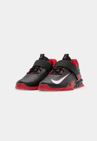 Black and red athletic shoes with a textured upper, strap closure, perforations on the toe, and a white Nike logo on the side.
