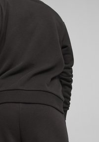 Felpa nera in pile con vestibilità rilassata, polsini e orlo a costine, realizzata in un tessuto texturizzato. Cuciture visibili attorno alle cuciture.