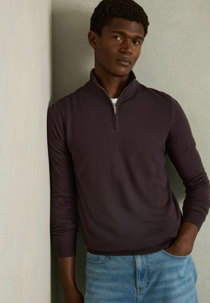 Pulover texturat de culoare maro închis, cu guler tip half-zip și mâneci lungi, asortat cu blugi din denim de culoare albastru deschis.