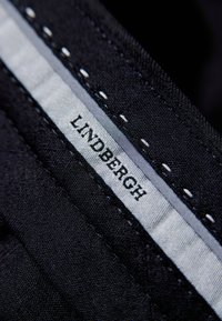 Zwarte stof met een gestructureerde afwerking heeft een wit label met "LINDBERGH" en grijze accentstiksels langs de rand.