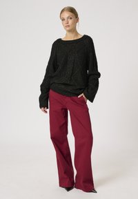 Sort strikket sweater med et tekstureret mønster, kombineret med højtaljede, bredbenede burgunderbukser og sorte spidse hæle.