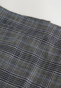 Harmaa ruudullinen kangas, jossa on sinisiä ja mustia yksityiskohtia, esittelee geometrisen tarkistuskuvion. Tekstuuri näyttää olevan kudottu ja valmistettu pehmeästä materiaalista.