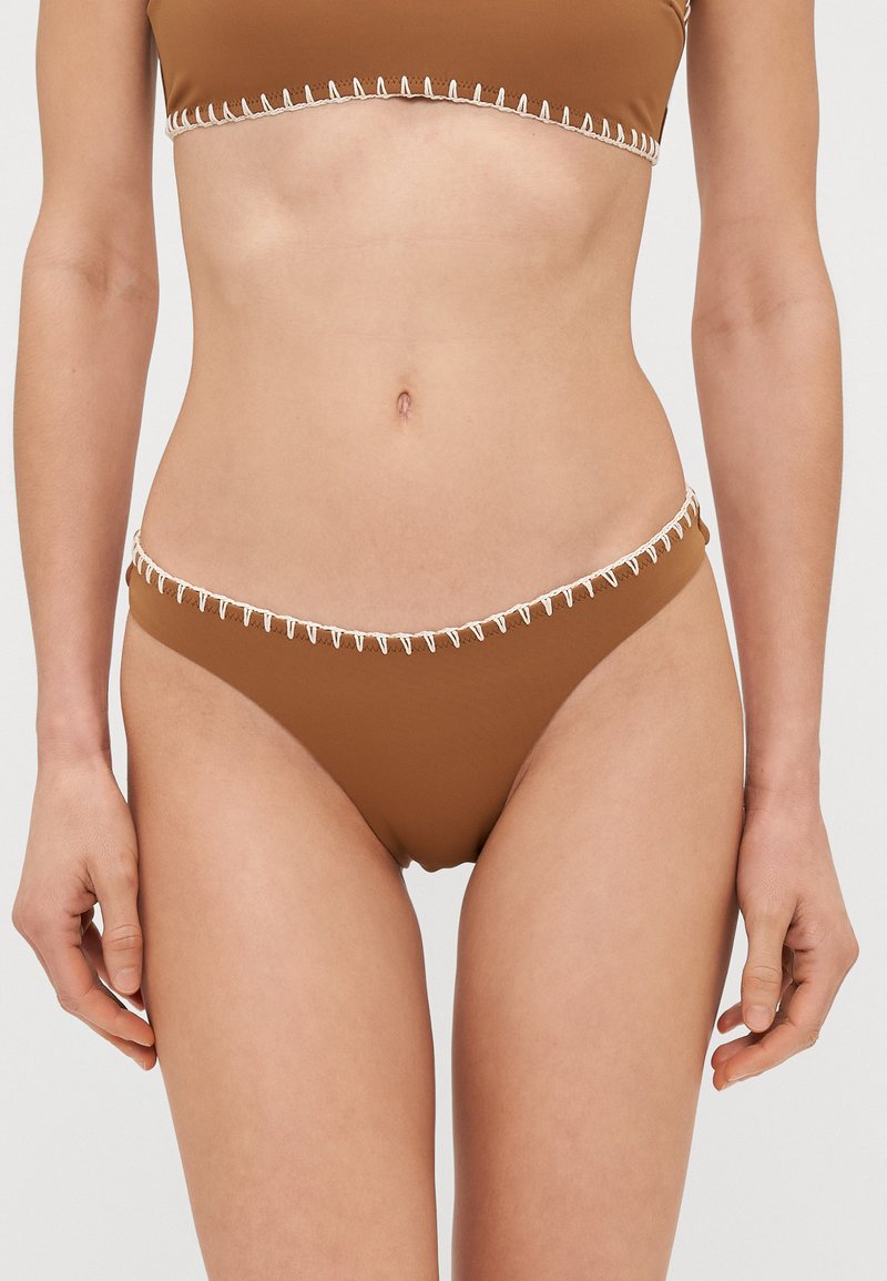 Rudos bikini kelnaites su lygiu paviršiumi ir grietinėlės spalvos siūlėmis palei juosmenį. Žemas liemuo, minimalus uždengimas.