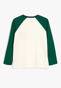 Długi rękaw T-shirt o kremowym kolorze z ciemnozielonymi rękawami raglanowymi, z okrągłym granatowym dekoltem i miękką bawełnianą teksturą.