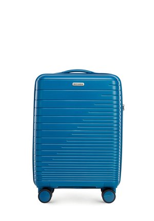 Hard-shell suitcase in blue with vertical ridged design, featuring a top handle, zipper closure, and four black wheels for mobility.
