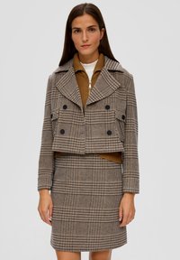 Dwurzędowa krótka kurtka w brązowo-beżowym kratkowanym wzorze, z czarnymi guzikami i klapami, w komplecie ze spódnicą w tym samym wzorze.