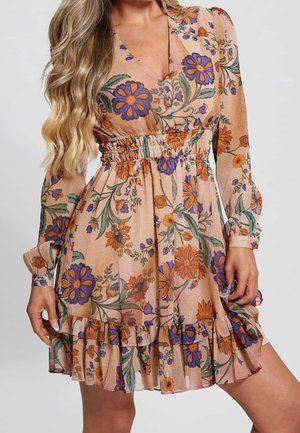 Femme portant une robe fleurie couleur pêche avec des fleurs violettes et orange, manches longues, ourlet à volants et taille froncée.