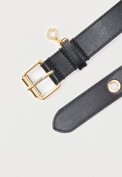 Μαύρη δερμάτινη ζώνη με χρυσή μεταλλική πόρπη, που διαθέτει διακοσμητικό χρυσό φυλαχτό και λεπτομέρεια με ροδέλα. Λείο υλικό με ραμμένα άκρα.