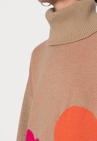 Beige Rollkragenpullover mit großen rosa und orangefarbenen kreisförmigen Mustern. Hergestellt aus einem strukturierten Strickstoff, hat er eine lockere Passform.