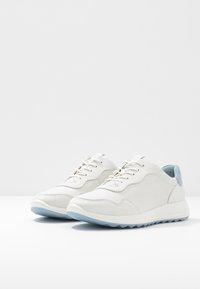 Sneakers bianchi con tomaia in pelle liscia, punta arrotondata, accenti blu sul tallone e suola in gomma testurizzata. Cinque occhielli per i lacci.
