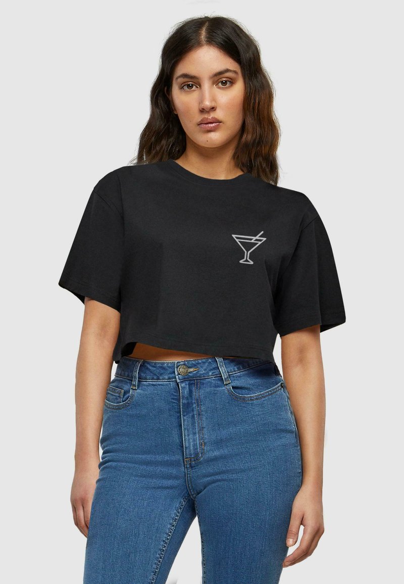 Tricou scurt negru din bumbac, având un grafic alb cu un pahar de cocktail în zona superioară stângă a pieptului. Asortat cu blugi din denim albastru cu talie înaltă.