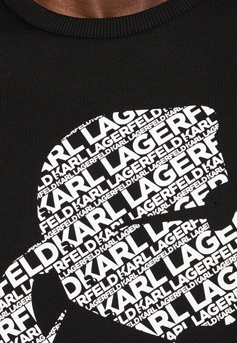 T-shirt nera a coste con una grande grafica bianca di testo sovrapposto che forma la scritta "Karl Lagerfeld", creando un audace motivo ripetuto.