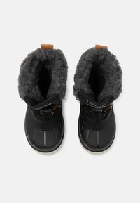 Schwarze wasserdichte Stiefel mit einer strukturierten Gummiaußenseite, grauem, flauschigem Innenfutter und braunen Lederakzenten am Zugschlaufe und Riemen.