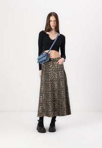 Schwarzes Langarmoberteil, gemusterter Maxirock mit Leopardenmuster und schwarze Knöchelstiefel. Das Model trägt eine blaue Umhängetasche.