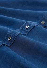 Tissu bleu foncé avec une texture douce, présentant des boutons-pression en métal le long du bord, et des plis délicats créant de la profondeur et de l'intérêt visuel.