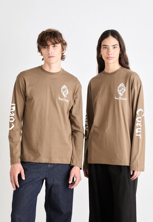 Brown long-sleeve t-shirts in cotton with white graphic details on the chest and sleeves. The fit is loose, complemented by dark denim pants.