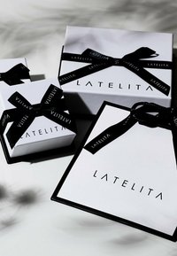 Tre scatole regalo bianche con nastro nero, che mostrano il logo "LATELITA" sul davanti e dettagli neri a contrasto.