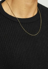 Collana in oro appoggiata su un maglione a maglia nera con texture. La catena è sottile e liscia, mettendo in risalto il suo design minimalista.