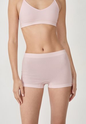 Shorts en coton rose clair, sans couture, avec une texture lisse et une taille élastique, conçus pour le confort et la flexibilité. Pas de motifs visibles.