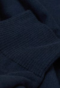 Dunkelblaues gestricktes Gewebe mit einem strukturierten Rippenmuster, das eine weiche und glatte Textur aufweist und Falten sowie Drapierungen zeigt.