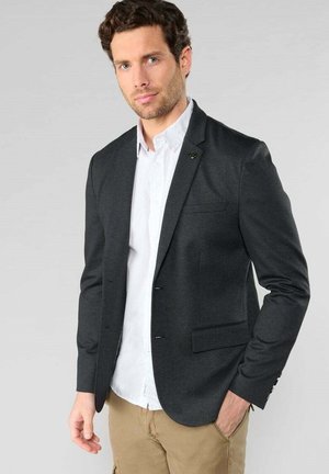 Donkergrijze blazer met een getailleerde pasvorm, enkele knoopsluiting en gelapte revers, gedragen over een witte blouse, met een gestructureerd materiaal en zijzakken.