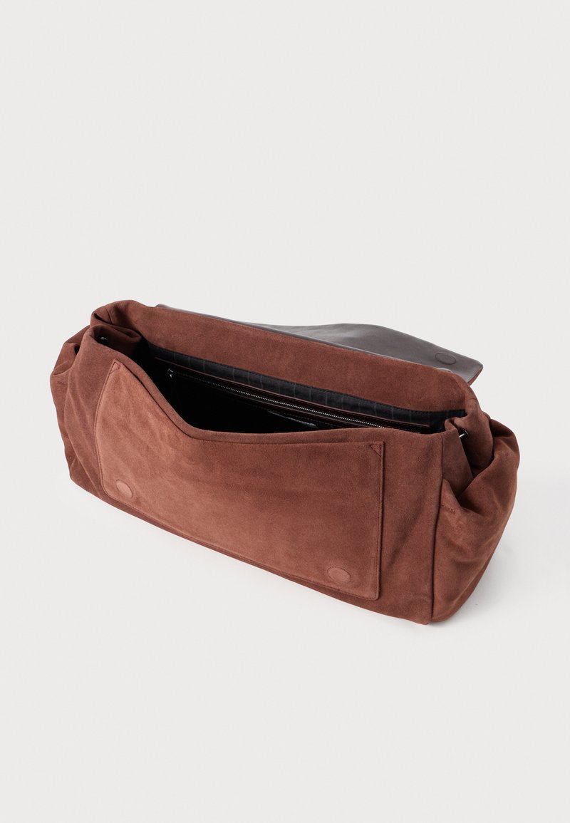 Bolso de ante marrón con una superficie suave y texturizada; presenta un cierre de solapa y un gran bolsillo frontal. Se ve un bolsillo con cremallera en el interior.