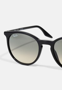 Ochelari de soare negri Ray-Ban cu lentile rotunde, cu gradient și un cadru din plastic elegant. Are un design minimalistic și logo pe lentila stângă.