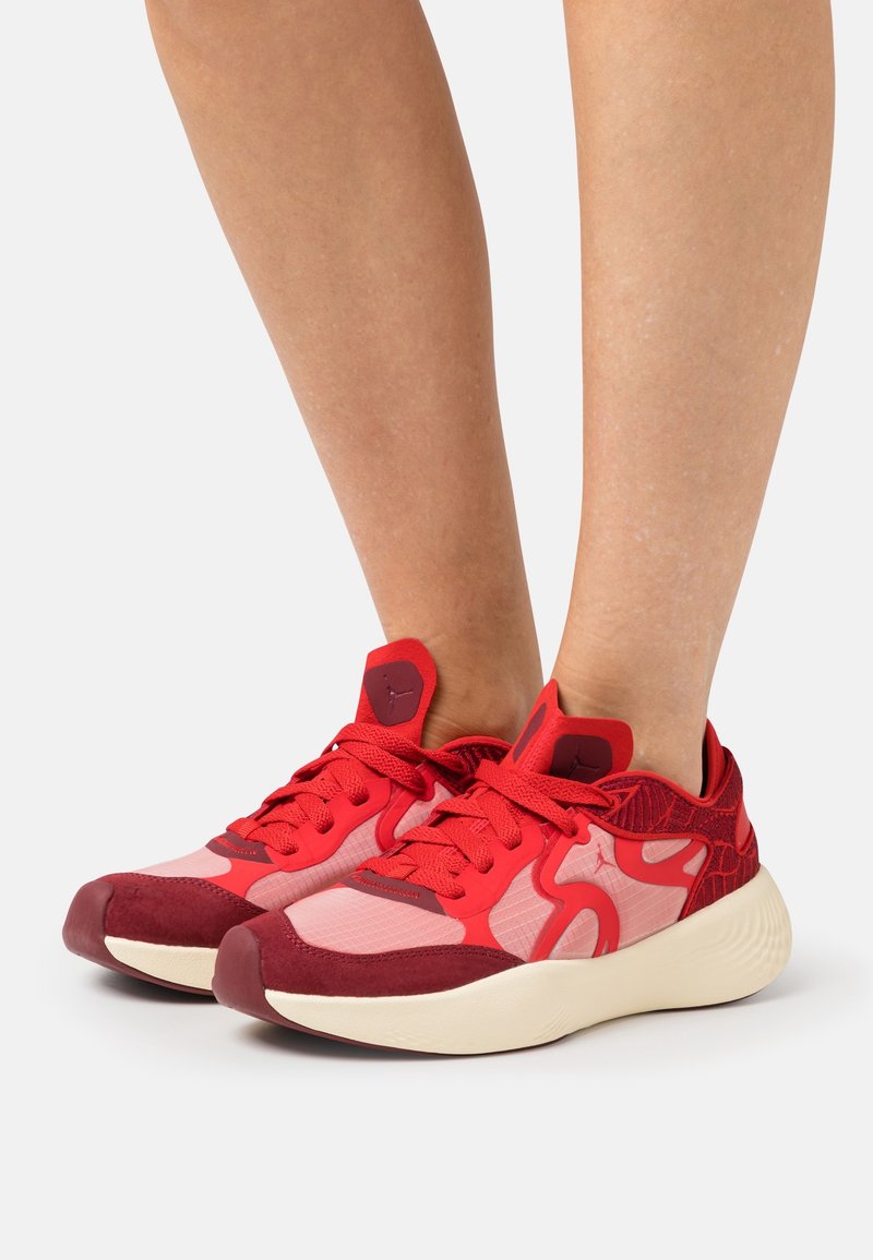 Des pieds portant des baskets rouges et roses avec des semelles blanches sur fond blanc.