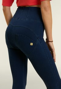 Leggings de mezclilla de alta cintura en azul oscuro, con una textura suave, bolsillos traseros y un pequeño logotipo de la marca en uno de los bolsillos.