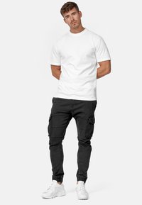 Camiseta blanca de algodón combinada con pantalones cargo negros que presentan múltiples bolsillos, piernas ajustadas y puños elásticos, completada con zapatillas blancas.