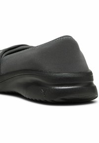 Musta liukusukki, jossa on sileä, matta pinta ja pyöristetty korko. Sisältää hienovaraisia ompeleita ja pehmustetun, teksturoidun ulkopohjan pitävyyden takaamiseksi.