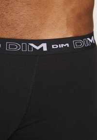 Schwarze Boxer-Briefs aus einem weichen, dehnbaren Stoff; ausgestattet mit einem breiten elastischen Bund mit dem weißen "DIM"-Logo. Glatte Textur mit enganliegendem Design.