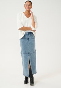 Langer, hellblauer Jeansrock mit einem vorderen Schlitz, kombiniert mit einem flauschigen weißen V-Ausschnitt-Pullover. Schwarze Knöchelstiefel runden das Outfit ab.