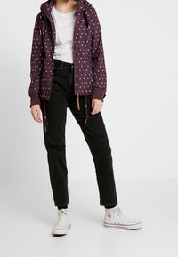 Lila mönstrad jacka med vita diamanter, justerbar huva, elastiska mudd, och dragsnören; tillsammans med svarta slitna jeans och vita sneakers.