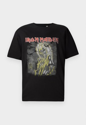 Melnas kokvilnas T-kreklas ar grafisku dizainu, kurā attēlota skeleta figūra ar dzelteniem akcentiem un teksts "Iron Maiden" sarkanā krāsā, apaļa kakla izgriezums.