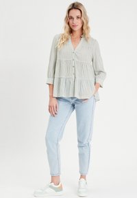 Chemisier à rayures vertes et blanches avec un design en étages, manches 3/4 et col, associé à un jean bleu clair et des baskets multicolores.