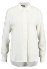 Bílá dlouhá košile s límečkem, texturovaná tkanina, zapínání na knoflíky vpředu a zakřivený lem. Hladký povrch s minimálními detaily.