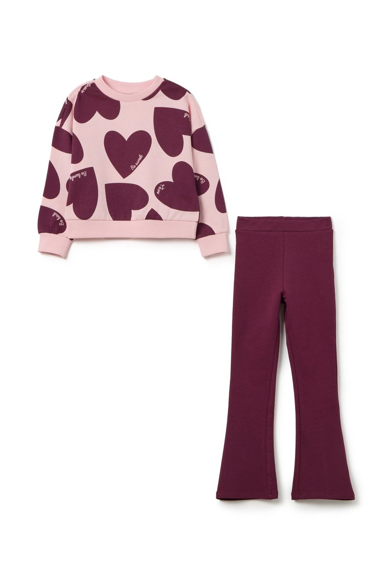 Roze sweater met grote bordeauxrode hartpatronen en de tekst "Be Loved", gecombineerd met effen bordeauxrode leggings. Beide gemaakt van zachte stof.