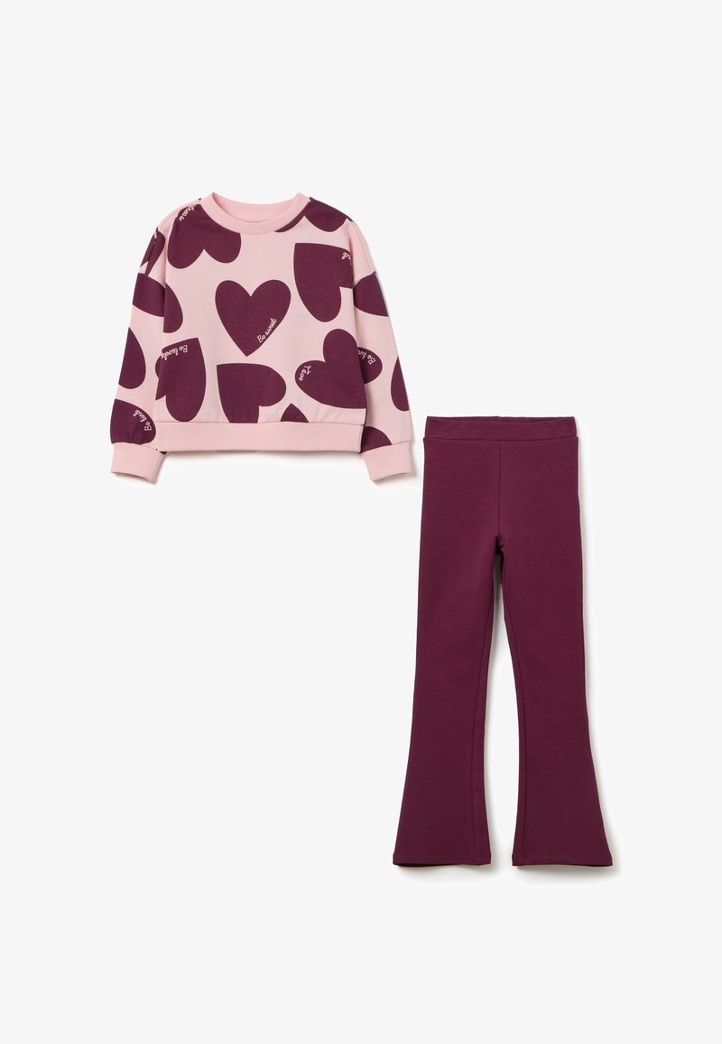 Roze sweater met grote bordeauxrode hartpatronen en de tekst "Be Loved", gecombineerd met effen bordeauxrode leggings. Beide gemaakt van zachte stof.