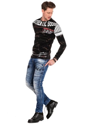 Chemise noire à manches longues avec des accents de texte blancs et rouges, associée à un jean léger en denim déchiré et des bottes noires lacées.