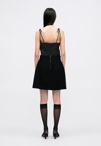 Μαύρο φόρεμα με ρυθμιζόμενες τιράντες τύπου spaghetti, εφαρμοστό κορσάκι, φουσκωτό φούστα, με φερμουάρ στην πλάτη, συνδυασμένο με μισό διάφανο καλσόν μέχρι το γόνατο και ψηλοτάκουνα.