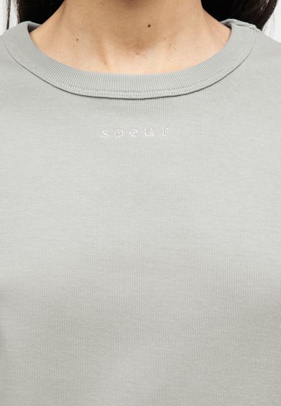 Ανοιχτό γκρι ριγωτό φούτερ με λαιμόκοψη τύπου crew. Μικρό κεντημένο κείμενο «soeur» σε ροζ χρώμα τοποθετημένο στρατηγικά στην περιοχή του στήθους.