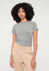 T-shirt grigio a maniche corte con design aderente, scollo rotondo e texture morbida, abbinato a pantaloni beige chiaro con una cintura larga.