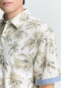 Chemise à manches courtes en tissu léger, ornée d'un motif de palmiers beige et marine, avec un col boutonné et des accents de poignet en chambray.