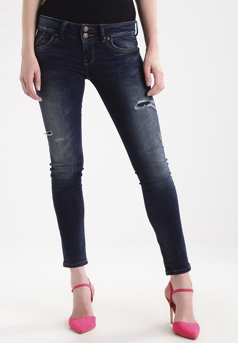 Jeans ajustados de color azul oscuro con detalles rasgados, que cuentan con un cierre de dos botones y costuras en contraste. Combinados con unos zapatos de tacón alto rosa.