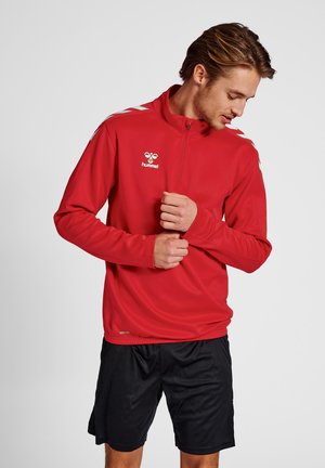 Rode sportieve zip-up jas met lange mouwen, met witte accenten en een logo. Draagt over zwarte shorts, die een gladde textuur tonen.